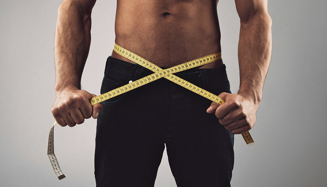 Fitness man measuring his body. Cropped and mid-section image of young man measuring his waist with tape measure against grey background. Health and fitness concept.