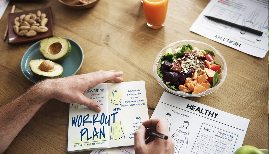 A person writing on a notepad beside a bowl of vegetable salad and a glass of orange juice, reflecting a health-conscious lifestyle.