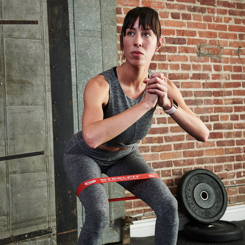 Woman squatting with red Mini Loop Band, ideal for targeting thighs and glutes. Durable, with five resistance levels for versatile workouts.