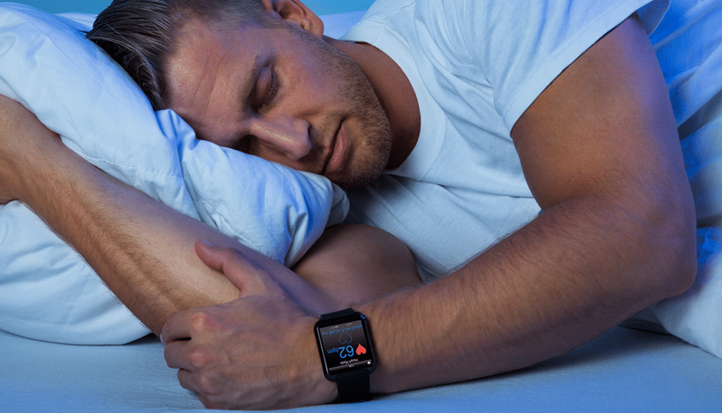 A man sleeps in bed wearing a smartwatch, highlighting lifestyle and wellness, aligning with SteelFit USA's focus on health and fitness goals.