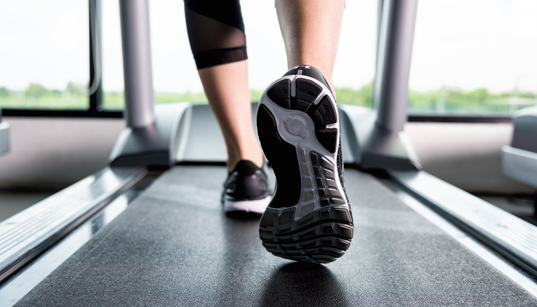 Close-up of a person's feet wearing black and white shoes on a treadmill, emphasizing fitness and exercise.