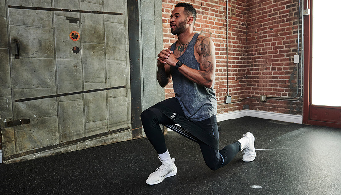 A man in a gym performing squats with hands together, showcasing fitness and strength, wearing casual athletic clothing and sneakers.