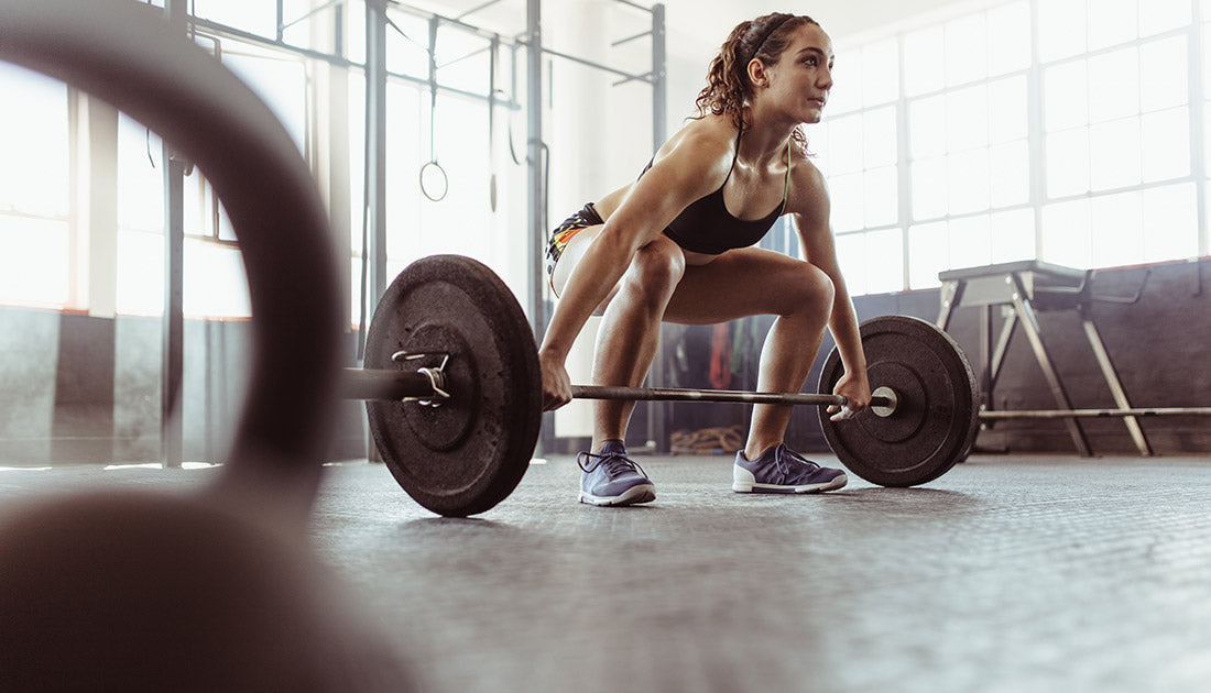 Young woman lifting a barbell at the gym. Fit female athlete exercising with heavy weights at cross training gym.