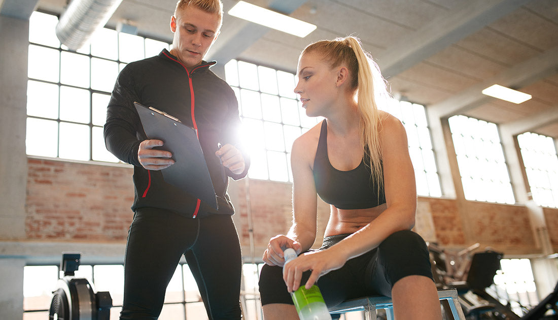 Personal coach standing near young woman and showing something on his clipboard. Female relaxing and talking with personal trainer after workout. Trainer making an exercise plan for young woman.