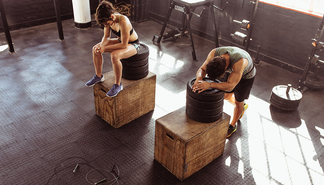 Fitness man and woman resting on box after exercises in cross training gym. Young people in the gym resting after heavy workout. Taking a break after intense physical training session.