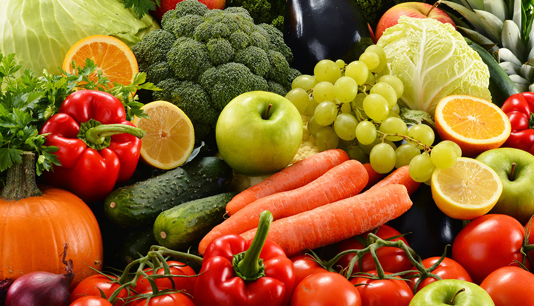 A close-up of assorted fresh fruits and vegetables, including apples, oranges, carrots, and tomatoes, highlighting natural, whole food nutrition.