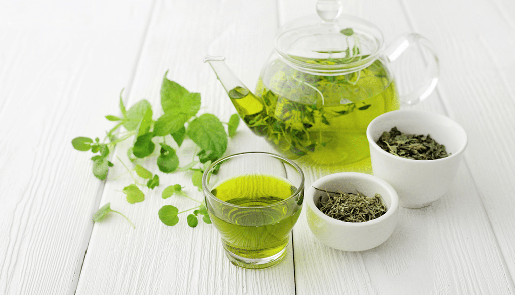 Glass teapot with green liquid and bowls of green leaves, suggesting a focus on health and wellness through natural ingredients.