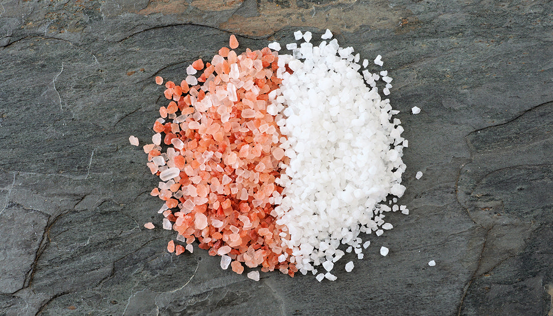 Close-up of white and pink salt crystals on a grey surface, illustrating natural elements often used in health and fitness products.