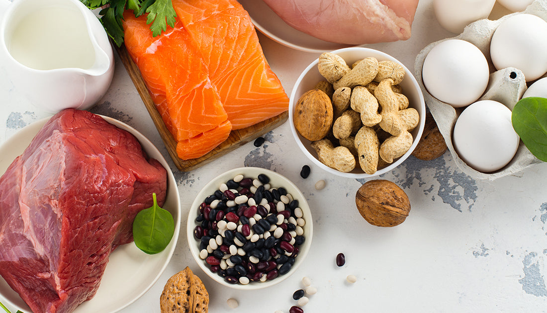 An assortment of foods including salmon, eggs, beans, and nuts, displayed in bowls and plates, emphasizing nutrition and health-focused ingredients.