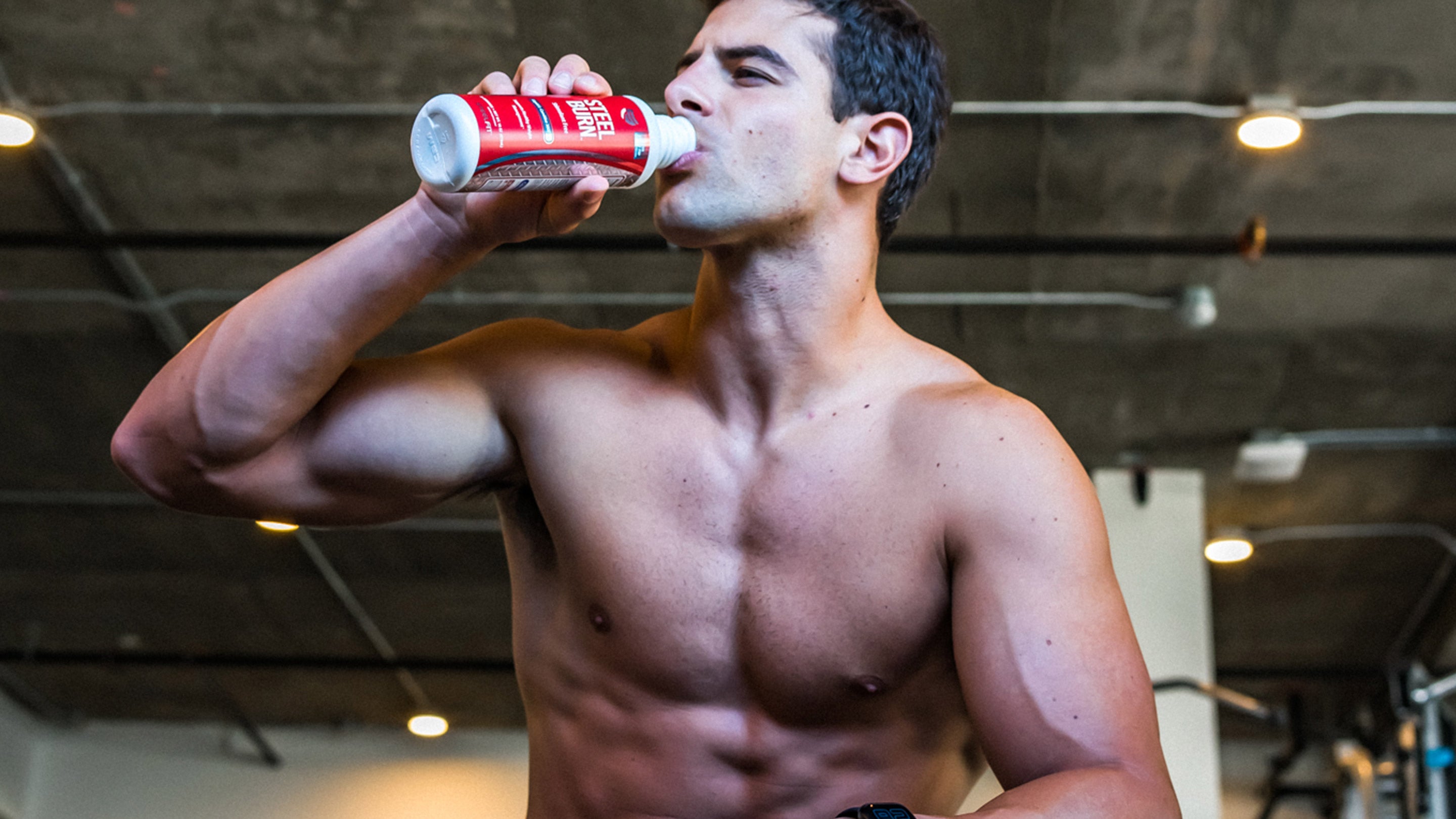 A bare-chested man drinks from a bottle, holding a red can, reflecting fitness and hydration themes associated with SteelFit USA products.