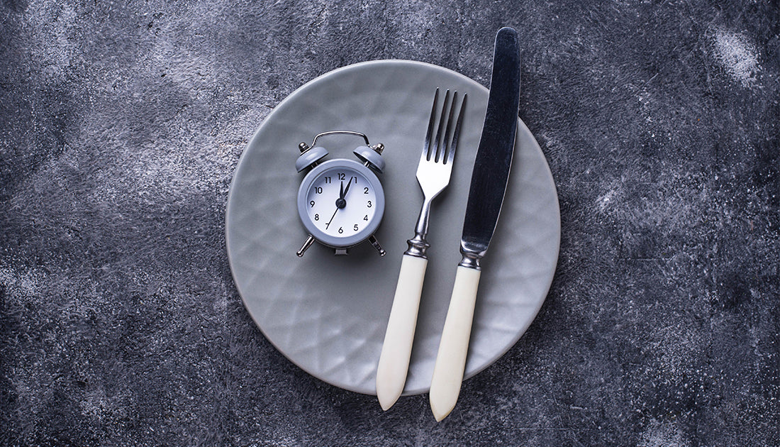 An alarm resting on a plate next to a fork and knife representing intermittent fasting