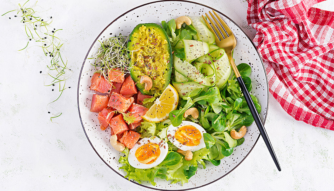 Plate of salad with avocado, tomato, and lemon slice, accompanied by a fork and spoon, representing fresh, nutritious meal options.