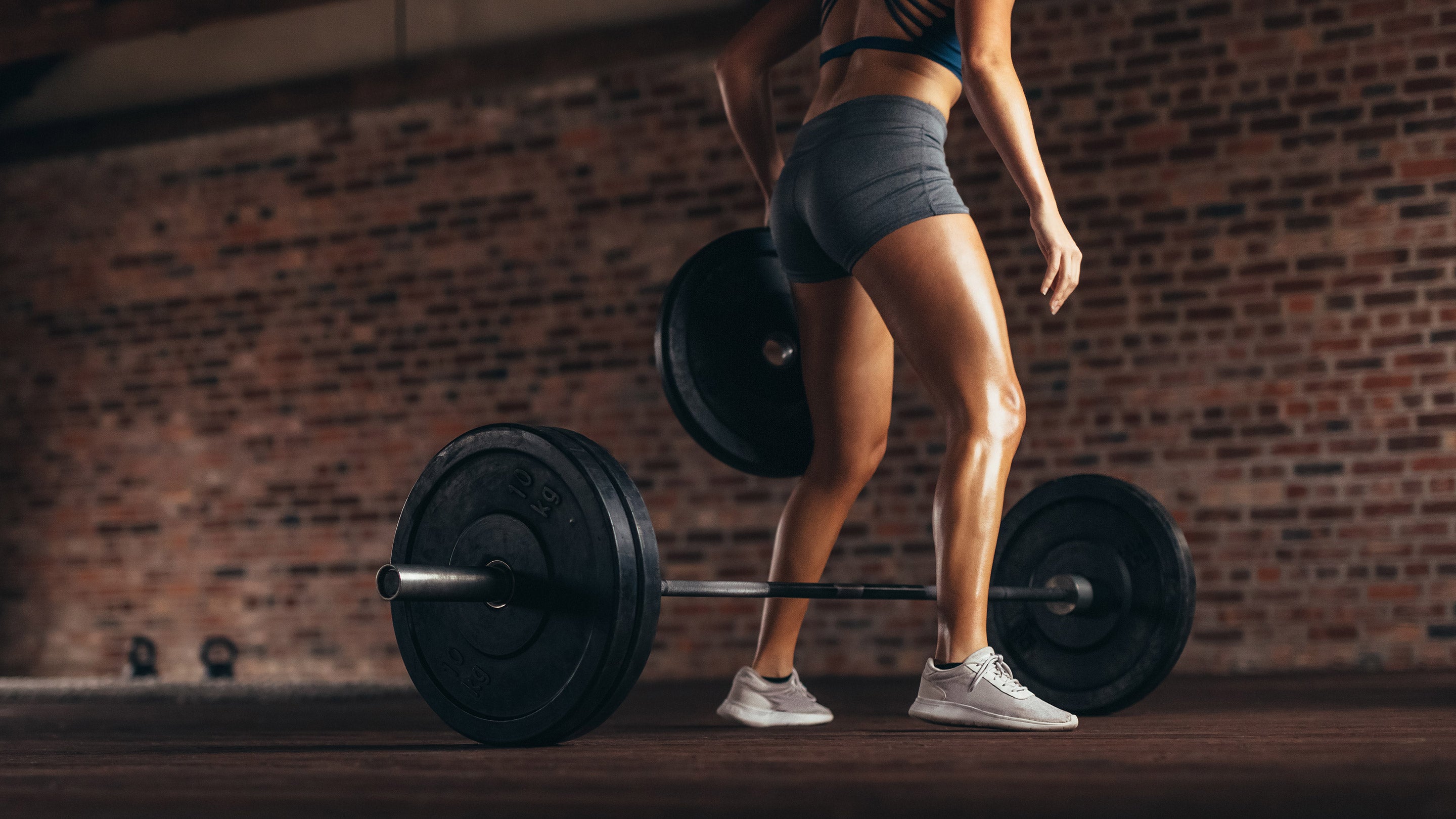 A woman lifting weights in a gym, focusing on strength training with barbells, reflecting dedication to fitness goals.