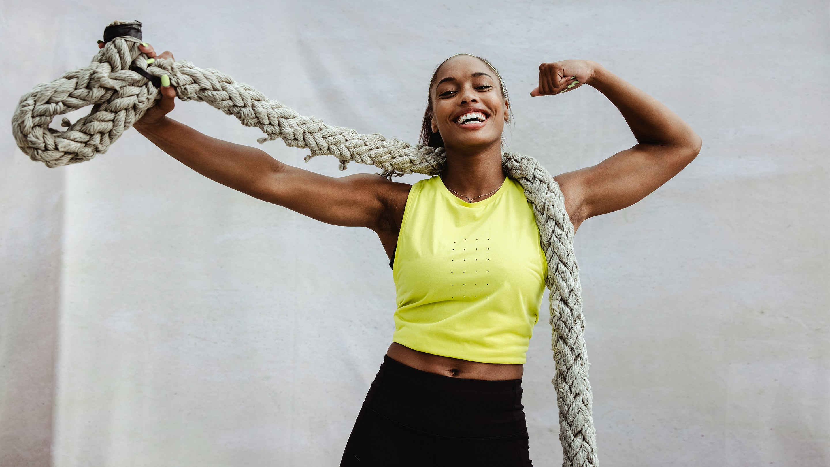 A woman in a yellow shirt holds a rope around her neck, smiling, suggesting fitness and strength, aligning with SteelFit USA's health and fitness focus.