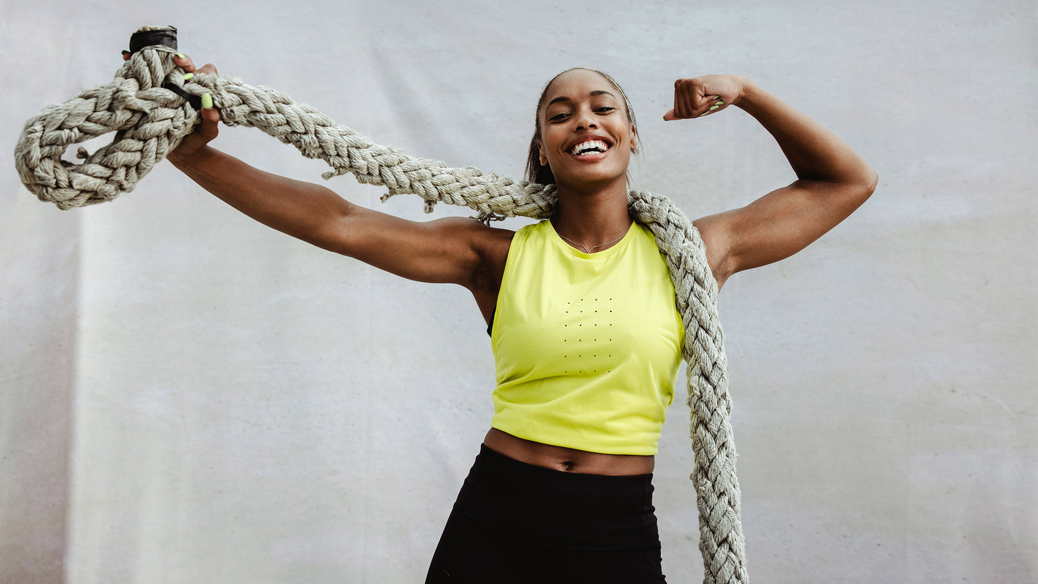 Strong African woman showing her muscular biceps with a battle rope. Fitness woman flexing arm muscles after cross training workout.