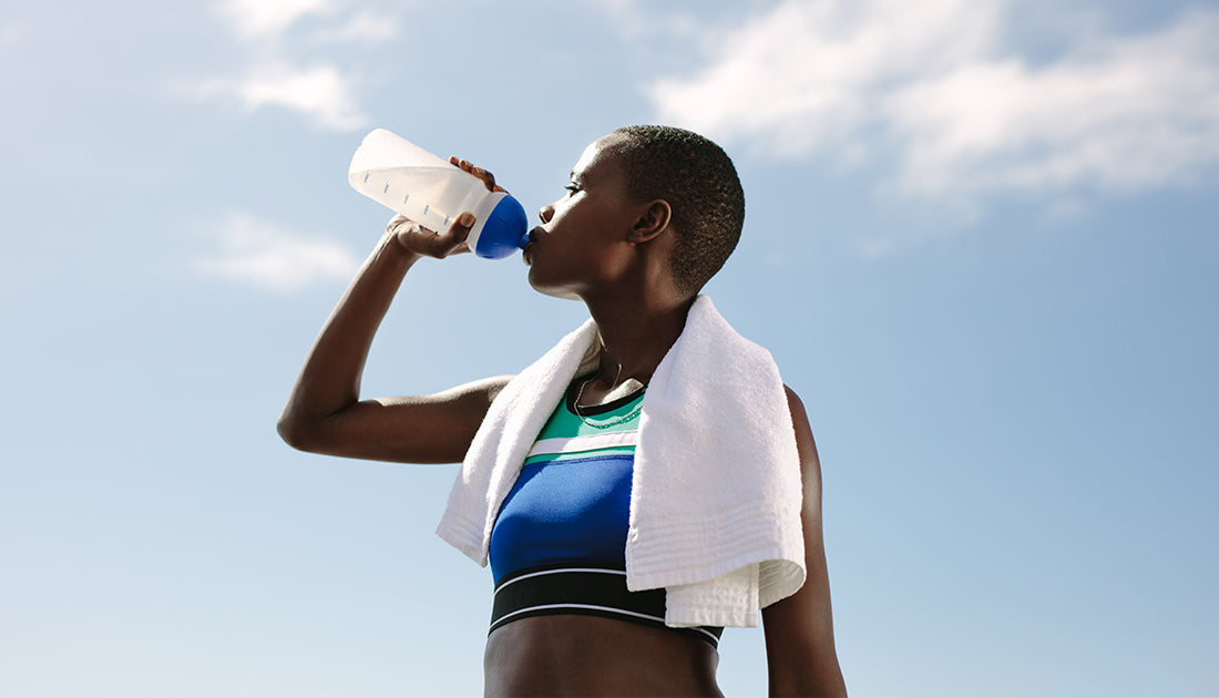 A woman outdoors drinks from a plastic bottle, embodying hydration and fitness, aligning with SteelFit USA's health and wellness focus.