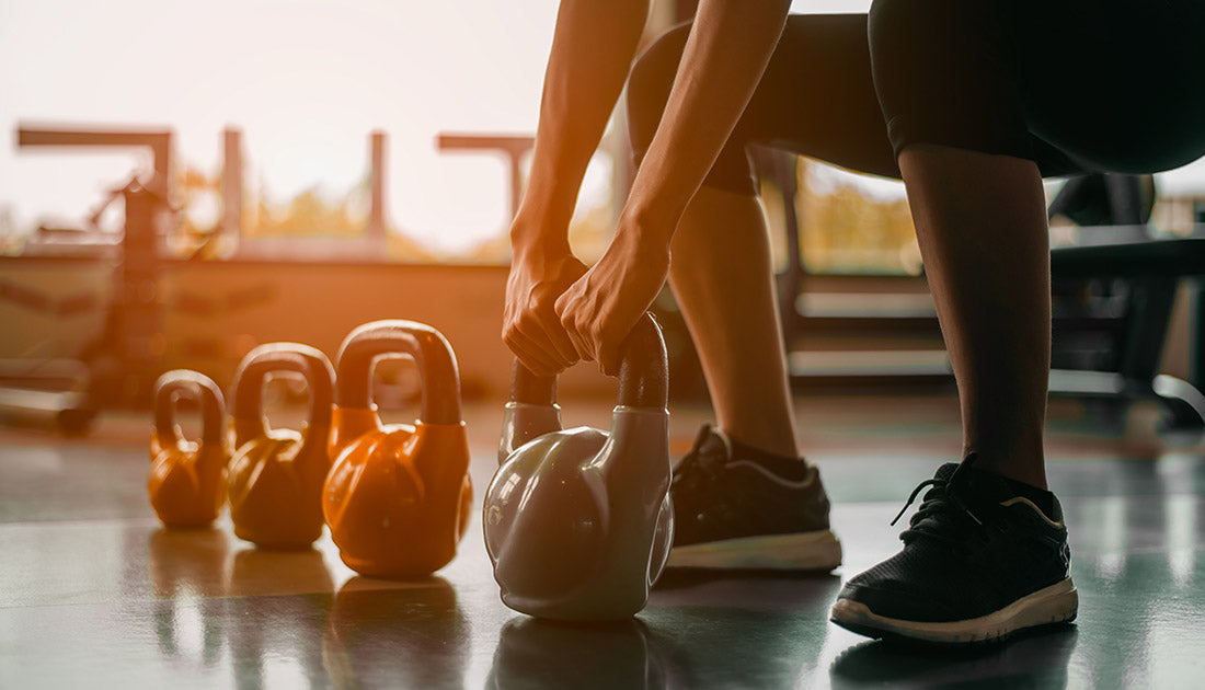 A person holding an orange kettlebell indoors, emphasizing fitness equipment, with a focus on footwear suitable for workout activities.