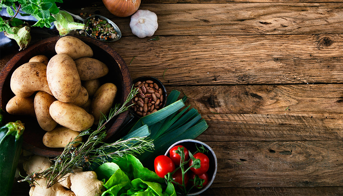 A bowl of fresh vegetables and spices, including tomatoes and beans, on a wooden surface, emphasizing natural nutrition.