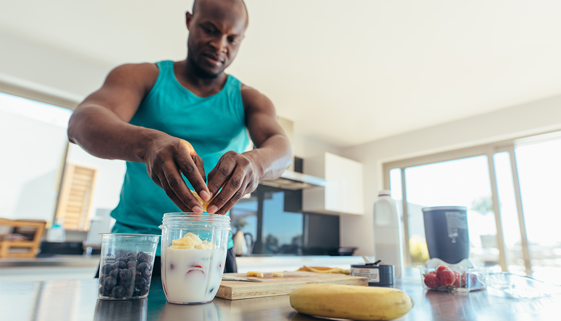 Muscular man putting chopped bananas into protein shake