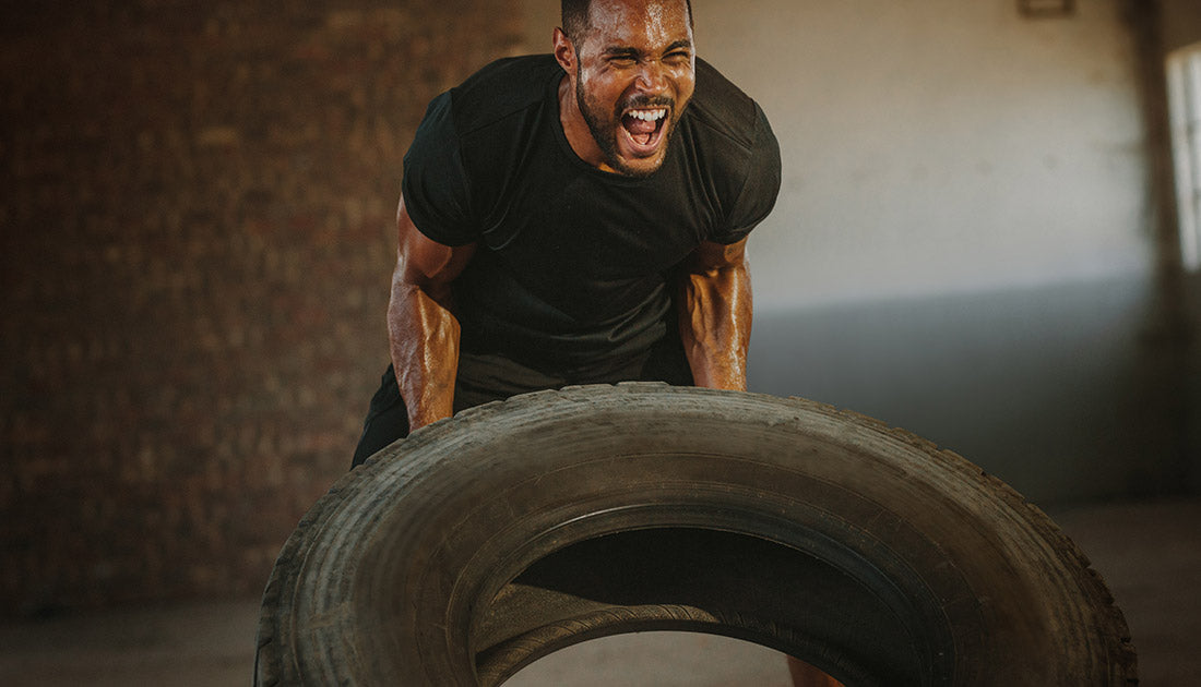 Male athlete flipping heavy tire inside an abandoned warehouse. Strong man flipping a tyre during an intense training session in a cross workout space.