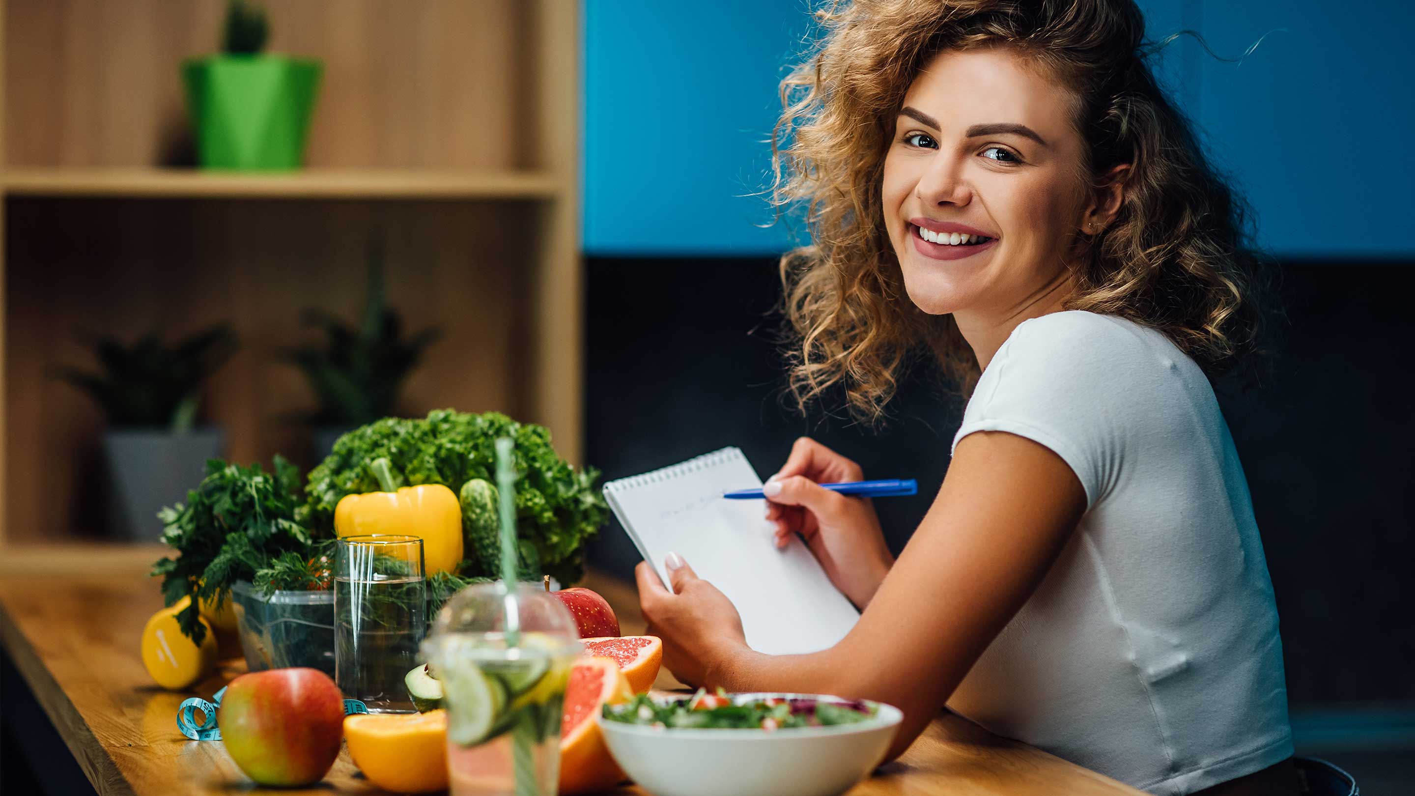 A woman writing on a notepad, with a bowl of salad and an apple nearby, reflecting a healthy lifestyle focus.