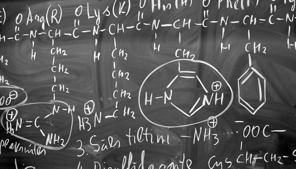 A blackboard with white chalk writing, featuring formulas and molecule diagrams, suggesting focus on scientific and nutritional analysis related to fitness goals.