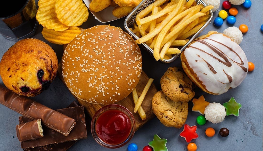 Assorted fast food items including a sesame seed burger, fries, donuts, a muffin, and a bowl of ketchup.