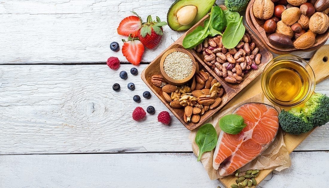 A table with diverse foods including salmon, broccoli, nuts, and grains, reflecting a balanced diet for health and fitness.