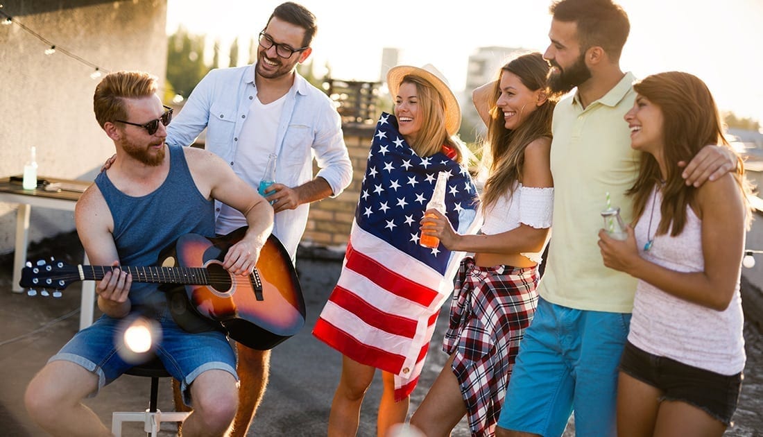 A group of people outdoors, including a man playing guitar and others enjoying drinks, reflecting a lively, social, and active lifestyle.