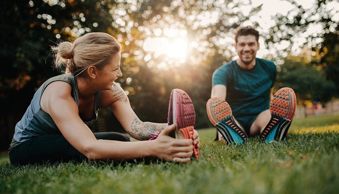 A man and woman stretching on grass, embodying fitness and wellness, aligning with SteelFit USA's focus on health and fitness goals.