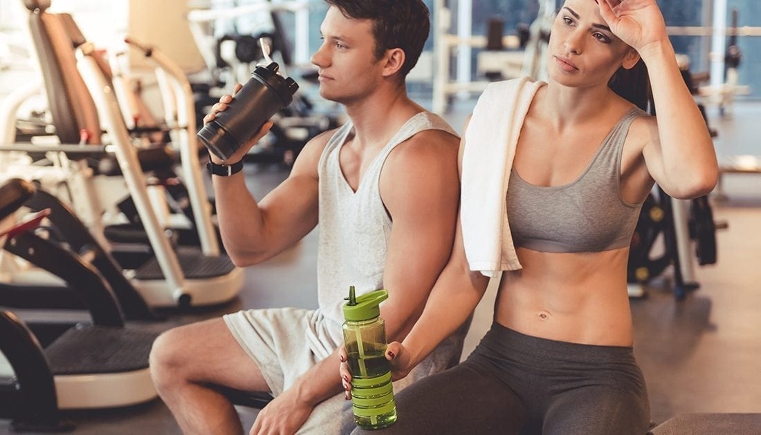 A man and woman sit on a gym bench; the man holds a shaker, reflecting fitness and nutrition themes aligned with SteelFit USA.