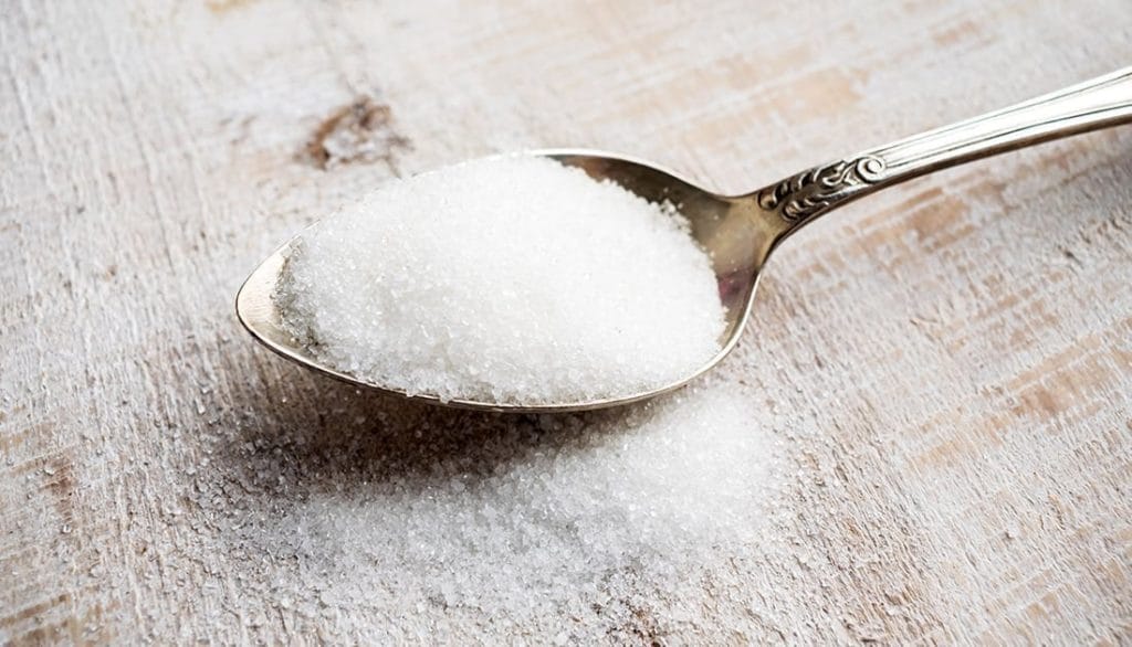 A spoon with a heap of sucralose sugar overflowing onto the counter