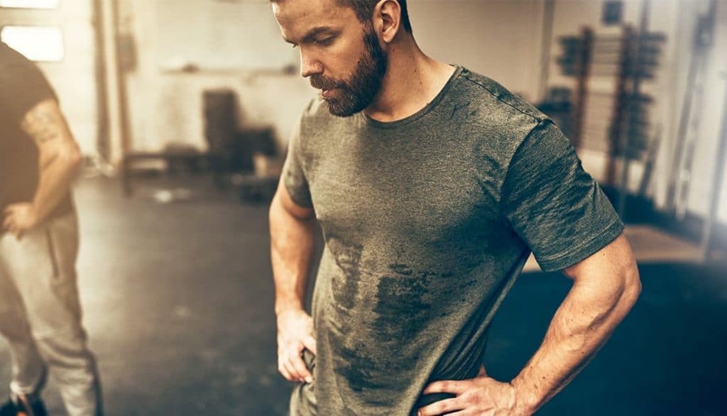 A man in a wet green shirt, highlighting muscle definition, possibly demonstrating the effectiveness of SteelFit USA's fitness topical creams.