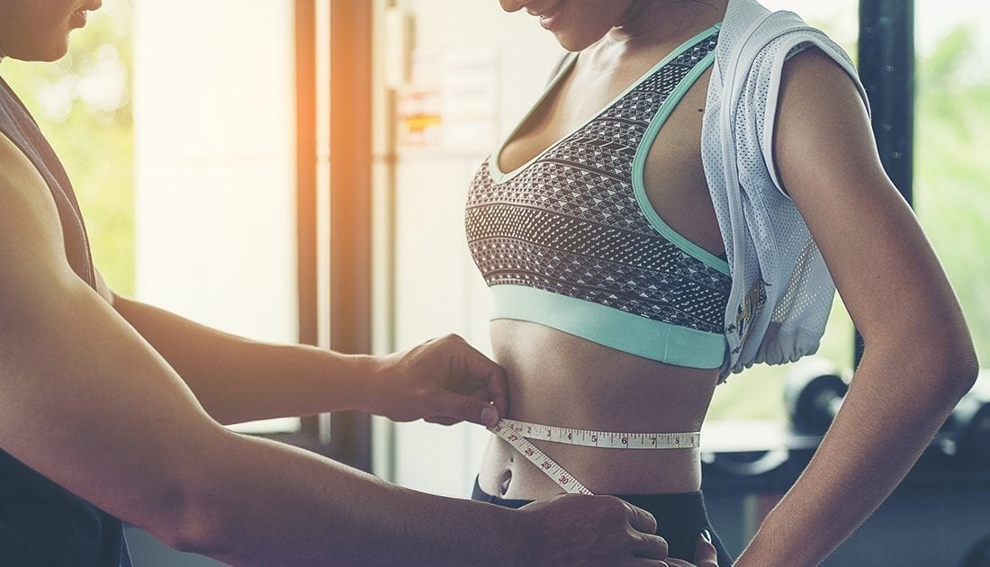 A person measures a woman's waist, emphasizing fitness and body measurement, aligned with SteelFit USA's focus on health and fitness goals.