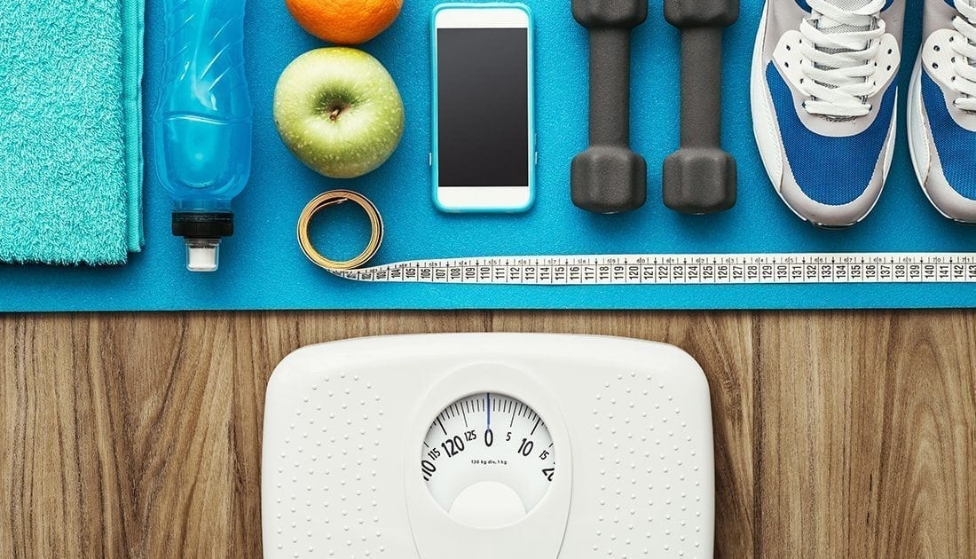 A weight scale, apple, and smartphone, reflecting a focus on health and fitness, associated with SteelFit USA's sports nutrition and wellness products.