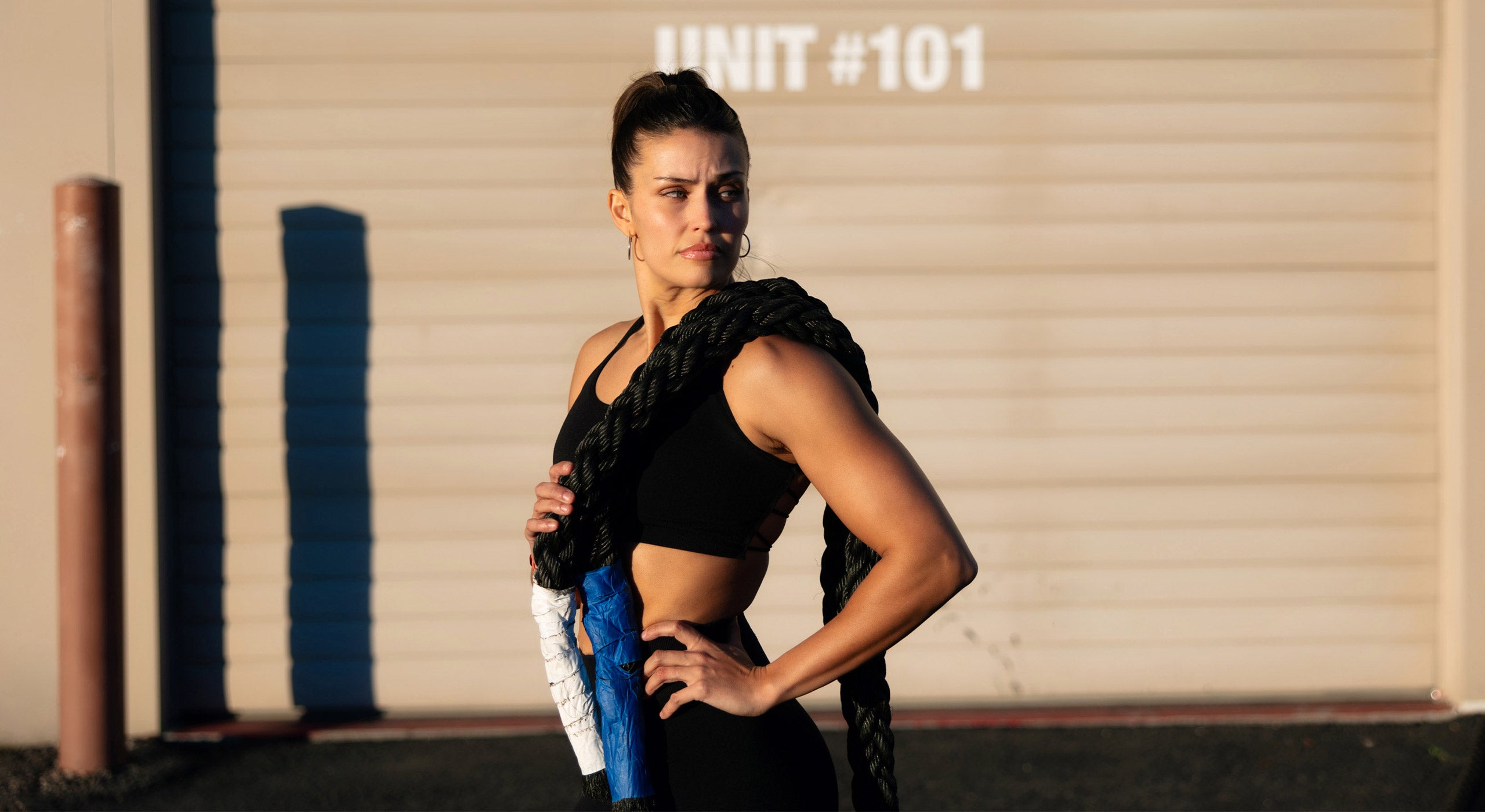 A woman in a black athletic outfit holds a rope over her shoulder, embodying fitness and strength, aligning with SteelFit USA's health and fitness focus.