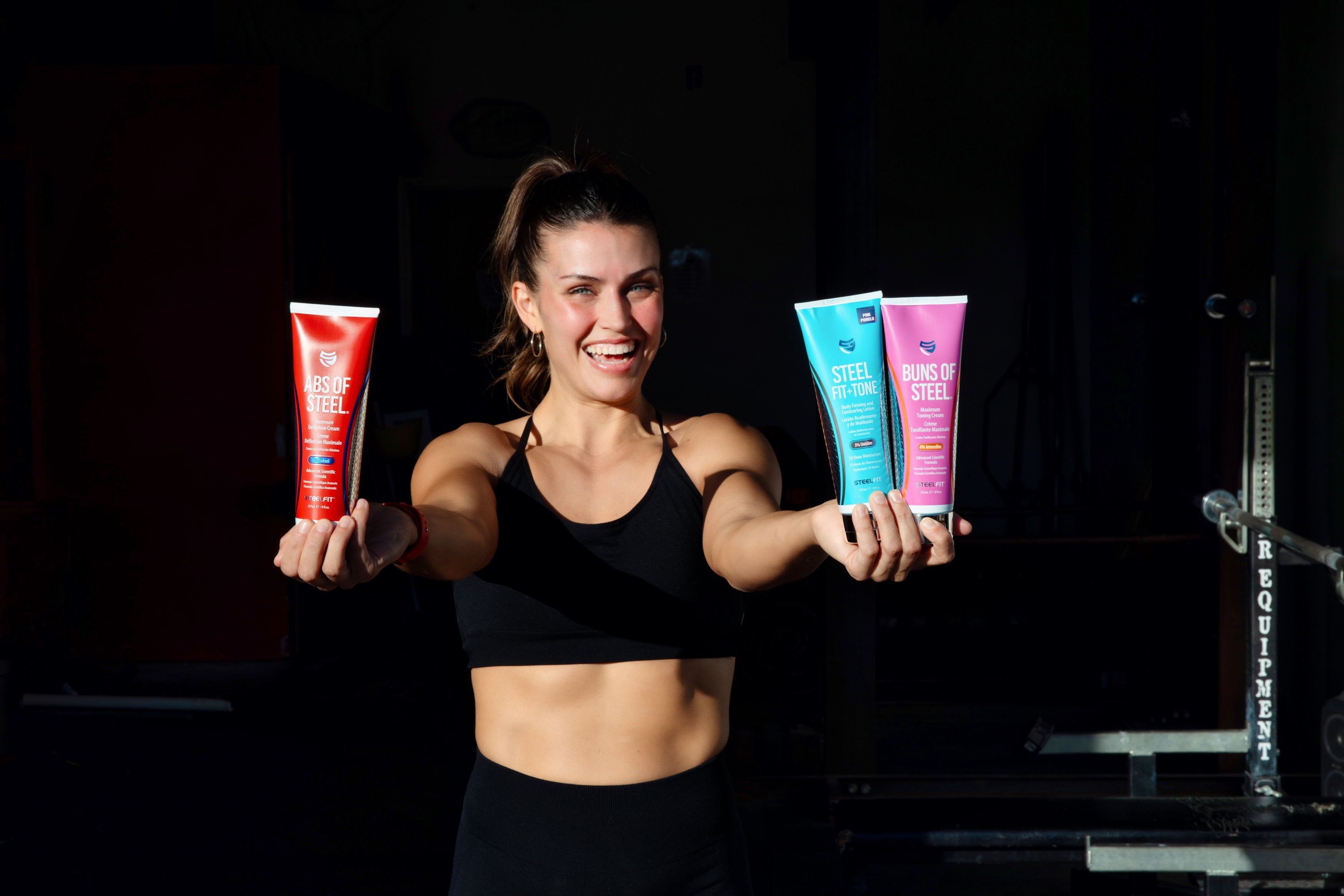 A woman holding two tubes of sports topical cream, smiling, reflecting health and fitness goals associated with SteelFit USA products.