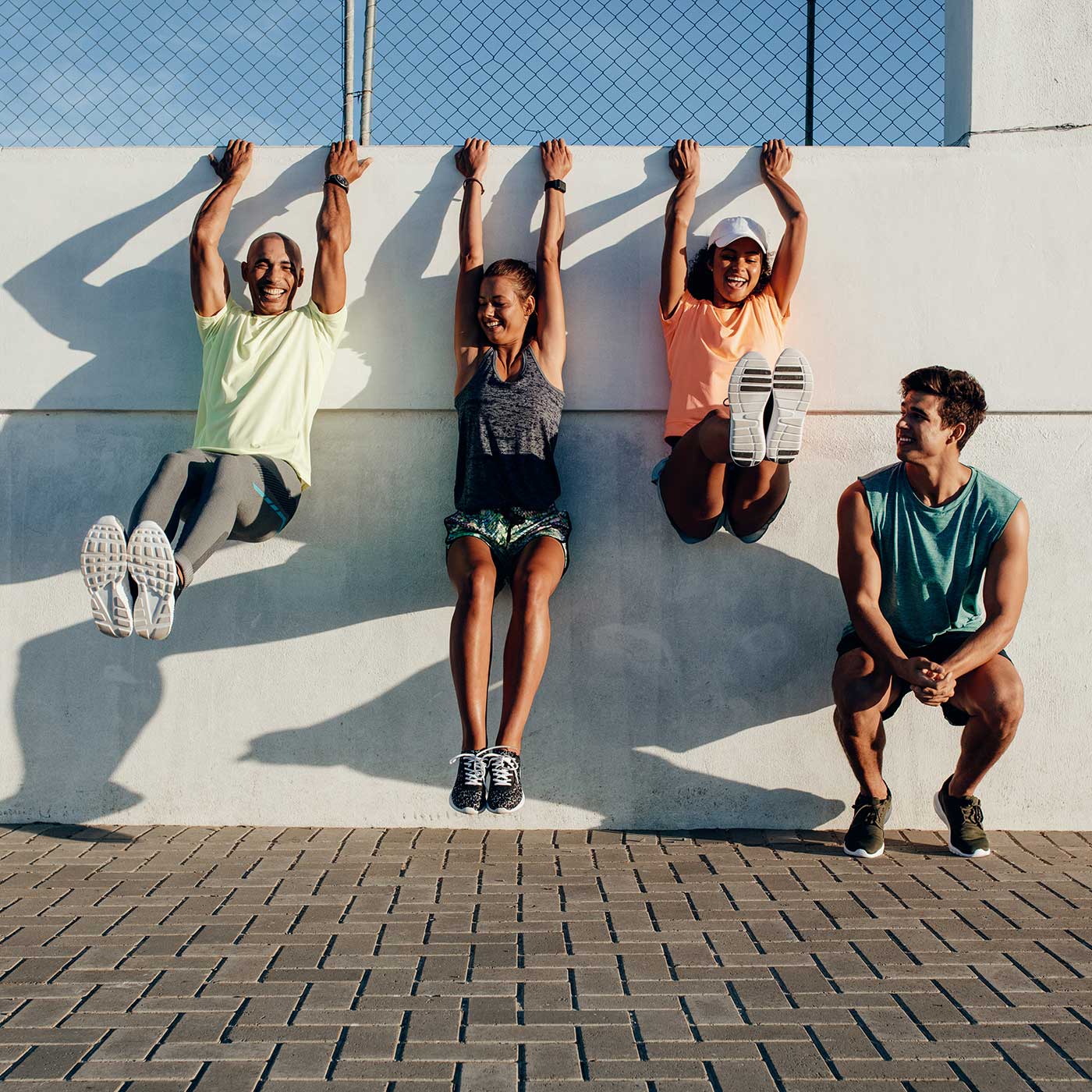 Group of people having fun during workout session outdoors. Friends hanging to a wall and stretching after running session.