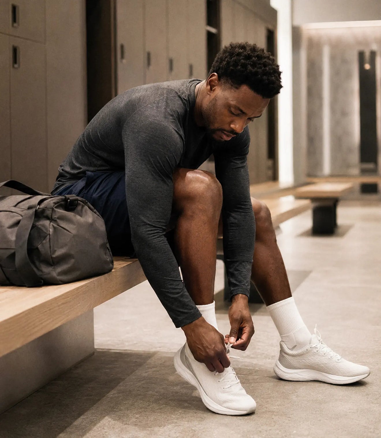 (Portrait) Informed Sport: A lean Black athlete, 30s, lacing his shoes on a bench in a clean modern locker room, plain gym bag beside him, calm pre-workout focus, soft overhead light.