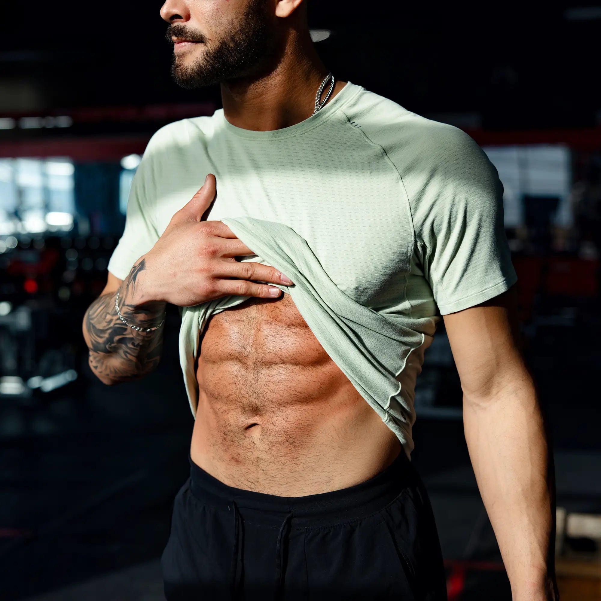 Man in a gym wearing a light green athletic shirt, revealing his abs.