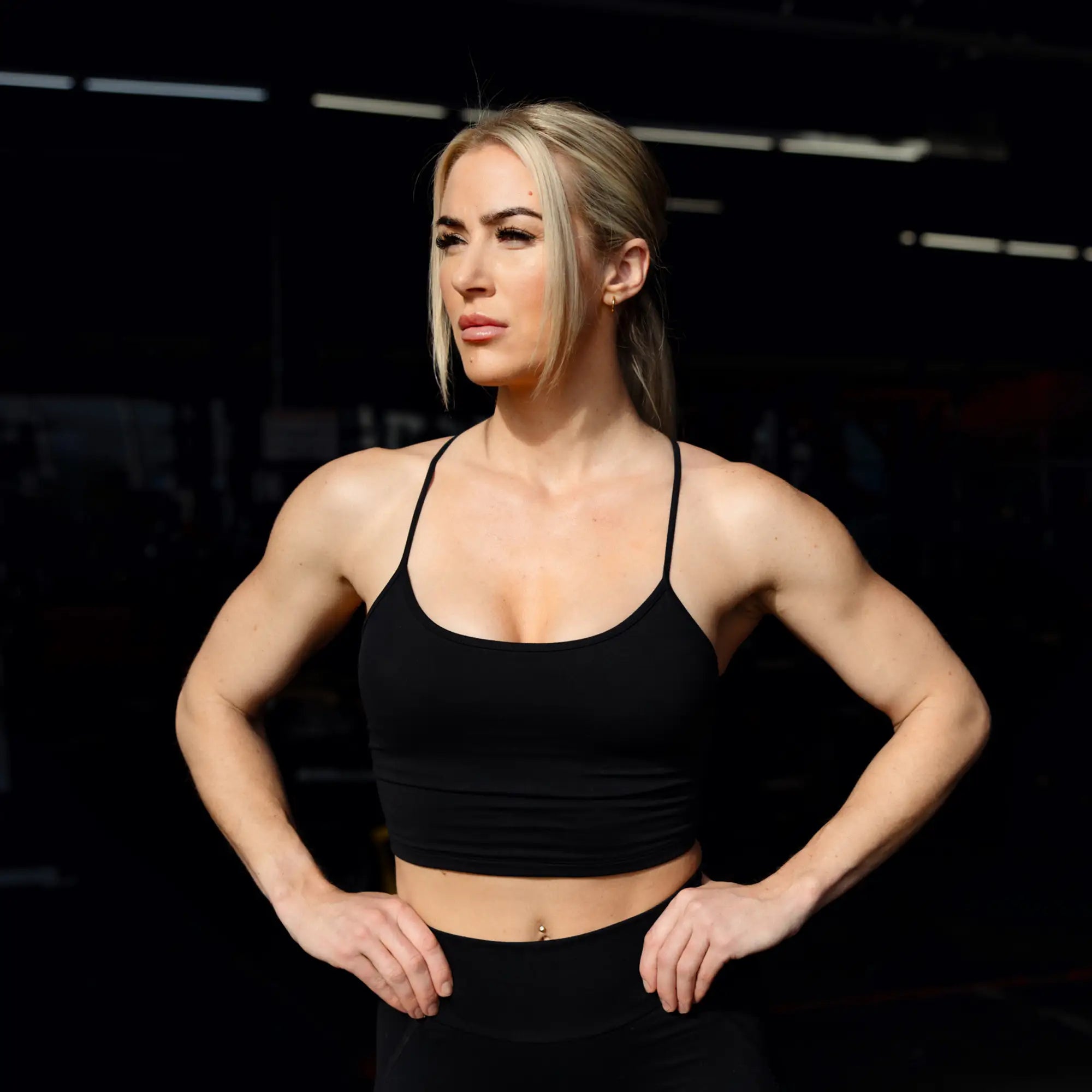 Woman in black athletic wear posing in a dark indoor setting