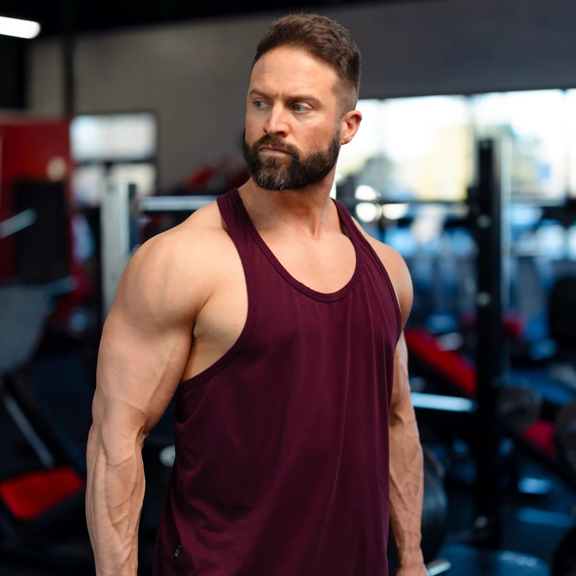 Man in a maroon tank top standing in a gym