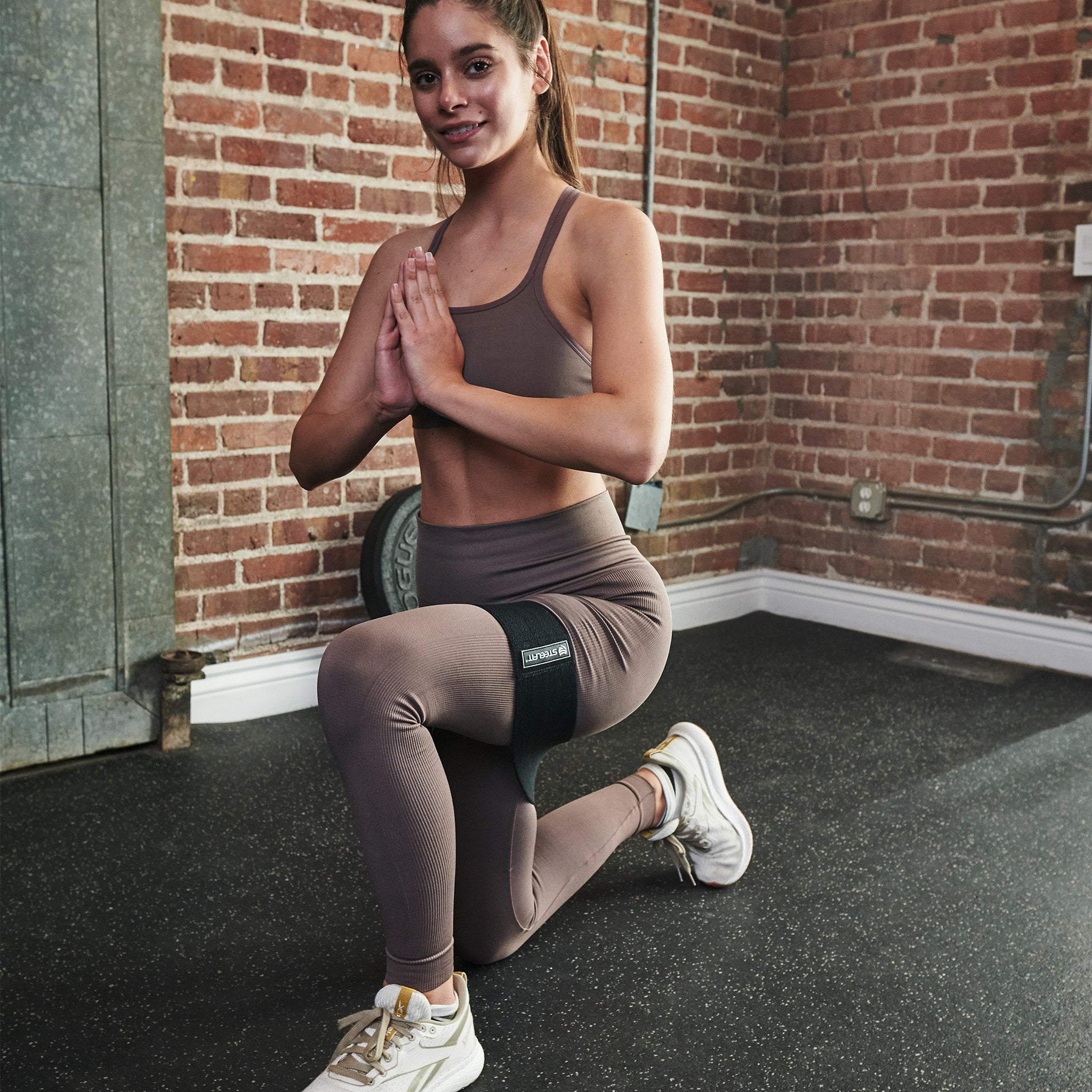 Woman squatting with a black hip band, demonstrating its use in resistance training for glutes and thighs.